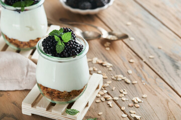 Yogurt with granola, blackberry berry fruits and muesli served in glass jar on wooden background. Healthy breakfast concept. Healthy food for breakfast, top view