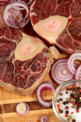 Raw fresh cross cut veal shank, red onion and pepper on kitchen board. Osso Buco on wooden cutting board