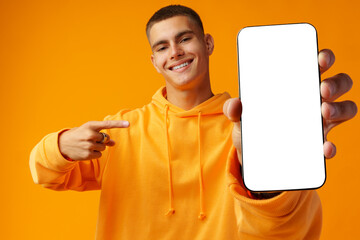 Smiling young man showing mobile phone blank white screen on yellow background