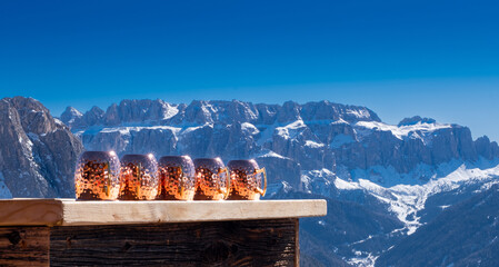 Ausblick auf umgedrehte Kupferbecher an einer Ski-Bar mit verschneiten Bergen im Hintergrund an einem sonnigen Wintertag