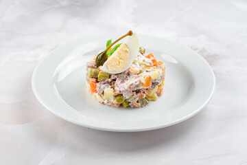 Russian salad olivier decorated dish on a white plate. Hearty salad of potatoes, carrots, peas, egg, cucumbers and mayonnaise