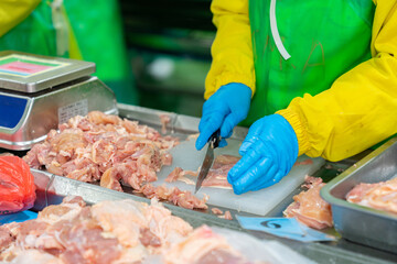 Hand of worker cut and trim chicken meat on cutting board from order sizing.