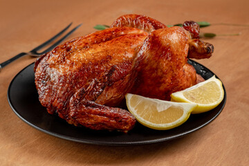 Whole roasted chicken with lemon slices served on a black plate. Oven-cooked chicken with a golden crust, close up