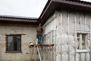 A man installs metal supports on the walls of the house for siding