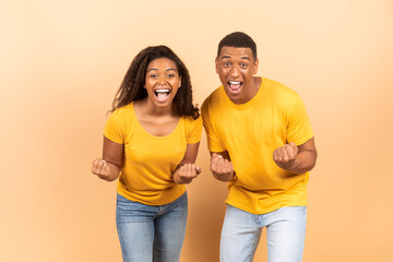 Fototapeta premium Hooray. Euphoric black spouses shaking clenched fists and exclaiming with excitement, celebrating success