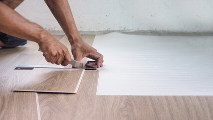 A technician is cutting luxury vinyl floor tiles with a cutter to lay the floor before placing it...