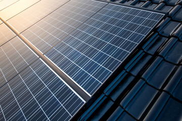 New solar panels are mounted on a roof with shiny black tiles and the clear sky is reflected in the...