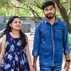Fototapeta premium Indian couple posing for maternity baby shoot. The couple is posing in a lawn with green grass and the woman is falunting her baby bump in Lodhi Garden in New Delhi, India