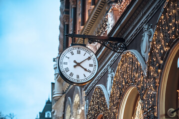 Retro street clock on the wall of old building decorated with lights for Christmas holidays in Kyiv city center.