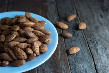 Selective focus on almonds on a white ceramic plate set on a rustic wooden floor.