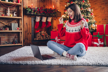 Full body portrait of excited positive lady sit cozy floor raise fists success online shop promo festive decoration lights indoors