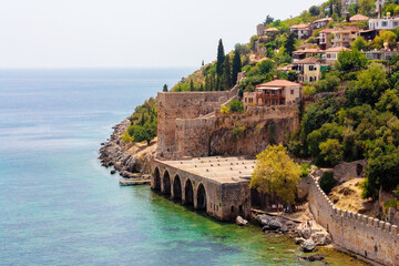 Fototapeta premium Ancient shipyard (Tersane) near of Kizil Kule tower in Alanya, Turkey (Turkiye) Famous tourist destination with high mountains. Beautiful beach and calm turquoise sea surface. copy space