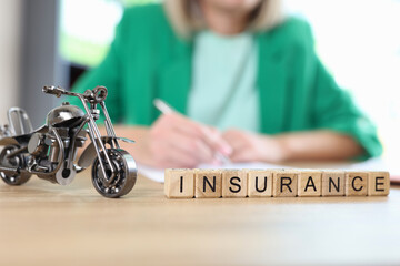 Motorcycle model and word insurance on table, blurred manager with documents in background.