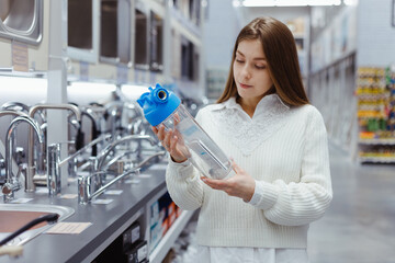 Woman holds household water filter for purification from mechanical impurities in hardware store.