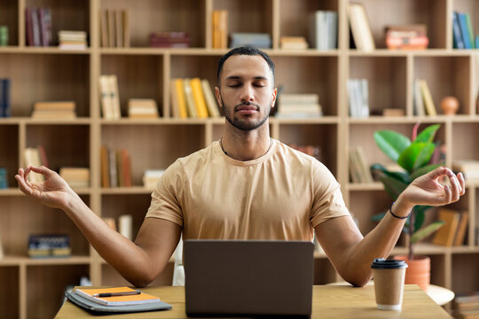 Workplace stress management. Calm arab man meditating with closed eyes in front of laptop, sitting at desk at home