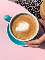 Young woman in silk dress is drinking latte art coffee. Young candid woman drinking morning coffee in tiffany color ceramic mug with saucer on cafe terrace.