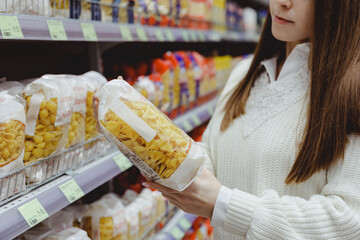 Young woman holds pasta package, shopping in grocery store.