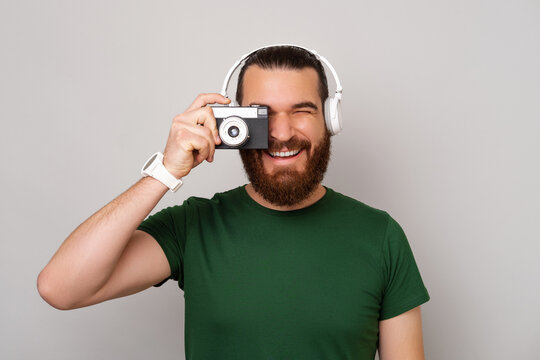 Bearded man wearing headphones and taking a picture with a vintage camera.