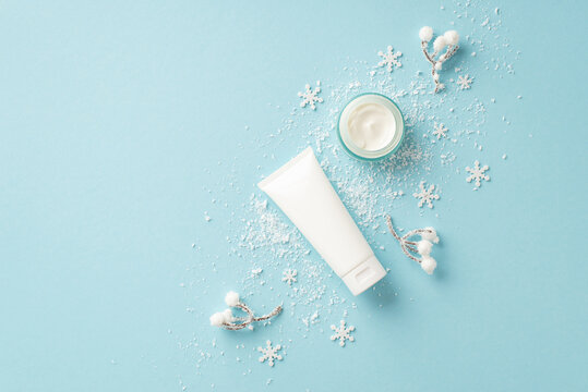 Winter Season Skin Care Concept. Top View Photo Of Cosmetic Jar White Tube Without Label Snowflakes Snow And Plant In Hoarfrost On Isolated Light Blue Background With Copyspace