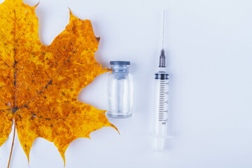 Autumn maple leaf and syringe with vaccine on white background. Vaccination against colds.