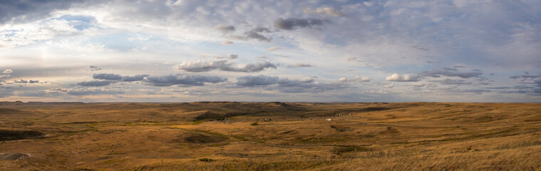 Fototapeta premium A distant campground in a dry treeless prairie setting under a sky with multiple shades of white and gray. 