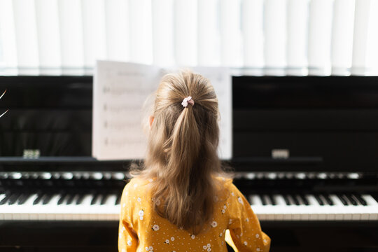 Little blond girl practicing music with the piano