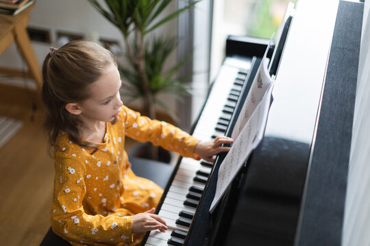 Little blond girl practicing music with the piano