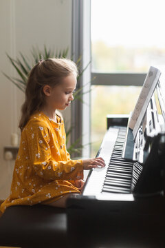 Little blond girl practicing music with the piano