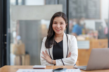 Asian business woman sitting with her arms crossed and confidently looking at the camera and focused on her work in the office.