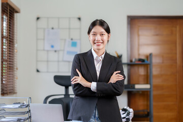 Asian businesswoman standing with her arms crossed and confidently looking at the camera and focused on her work in the office.