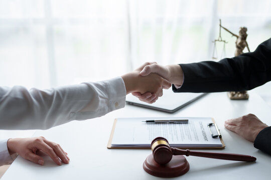 Lawyer shaking hands with a client making about documents, contracts, agreements, cooperation agreements with a female client at the lawyer's desk and a hammer at the table.