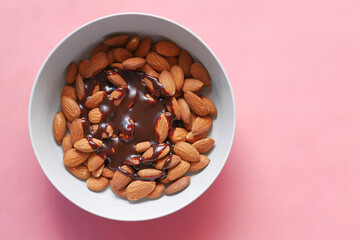 dark chocolate cream pouring on almond nuts in a bowl on pink 