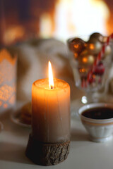 Glass with Christmas ornaments, cup of tea, cookies, candles and knitted blanket by the fireplace. Cozy Christmas at home.