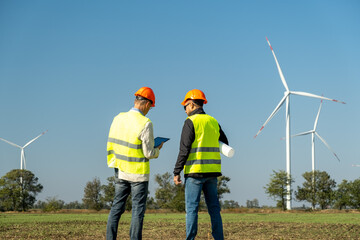 Engineers maintain contemporary windmills in countryside. Wind turbines rotate under cloudless sky. Professionals check operation of built wind farm