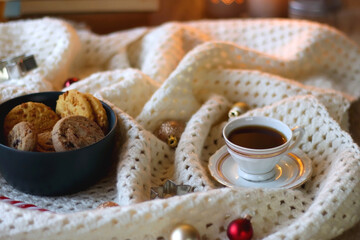 Cups of tea or coffee, bowl of cookies, soft blanket, lit candles, books and various Christmas decorations on the table. Selective focus.