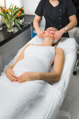 Soon-to-be mother spending her free time at skincare centre. Traditional Japanese face massage performed by unrecognizable caucasian specialist. Vertical indoor shot. High quality photo