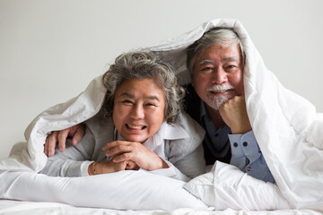Happy smiling asian elderly couple hugging and sleeping together in blanket on bed with white...