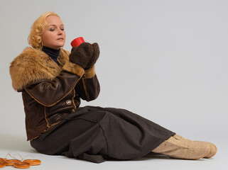 woman in a fur jacket sits with a red cup in her hands on a white background