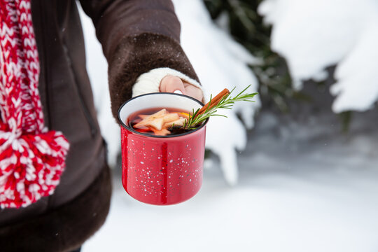 Mulled wine in red cup in female hands. Hot winter drink with wine, spices and fruit outdoor on snowy background. Copy space.