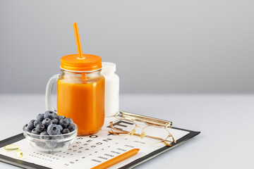 Glass of carrot juice bowl with blueberries, eye glasses and the Snellen table for vision testing on a white table. Nutritions for good vision. Vitamin A product to improve vision and reading, writing