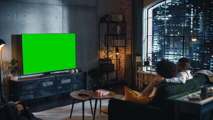 Black Couple Spending Time at Home, Sitting on a Couch, Hugging and Watching Exciting TV with Green...