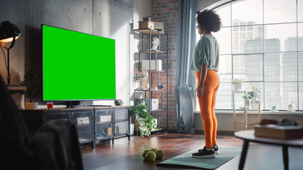 Home Gym: Gorgeous Positive Black Girl Training with Using Green Screen Mock-up TV. Authentic Woman Uses Workout Service Fitness App, Streaming Virtual Training with Chroma Key Television Set.