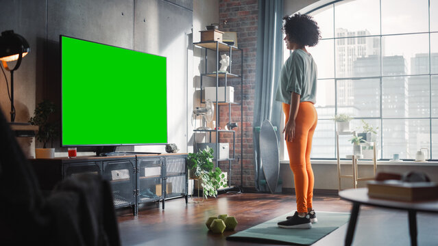 Home Gym: Gorgeous Positive Black Girl Training With Using Green Screen Mock-up TV. Authentic Woman Uses Workout Service Fitness App, Streaming Virtual Training With Chroma Key Television Set.