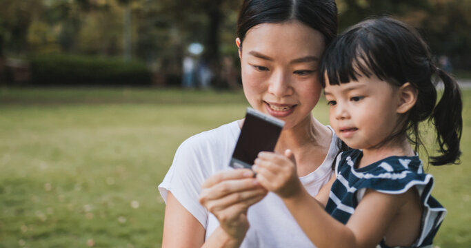 Young Asian mother hold cute daughter, look at polaroid photo picture with smile. Mom kid love relationship or happy child concept with copy space, lovely family together moment