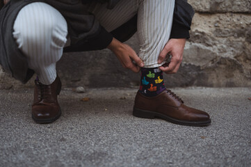 Man in elegant shoes pulling up colorful thumb up symbol socks on the street