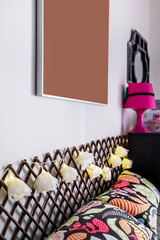 Bedroom corner with cushions, a dark chest of drawers and a pink lamp and flower garland with lights