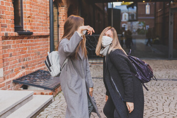 Young pretty girls friends in medical masks having fun outdoor in autumn evening in city laughing and going crazy - end of pandemic concept