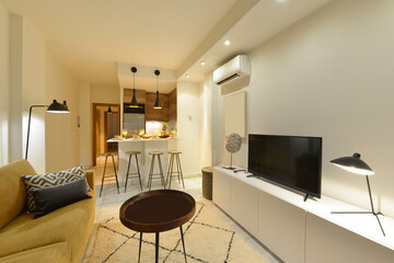 Living room decorated with a three-seater sofa in yellow fabric, a white patterned rug and a kitchen bar with high stools