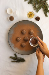 Homemade chocolate truffles, hands with strainer sprinkling cocoa powder and Christmas decoration