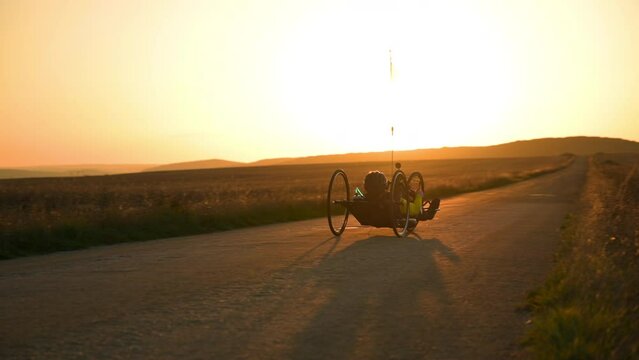 Scenic Shot of a Young Man Athlete with disability Riding a Handcycle. Adaptive Exercise Outdoors at Sunset . High quality 4k footage